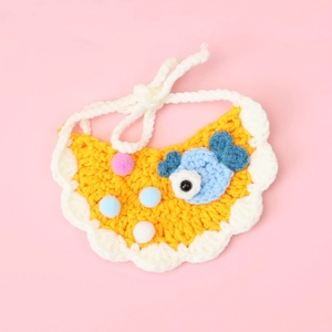 Detail of hand-knitted orange cat bib with blue fish patch and colorful pom-pom decor