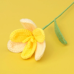 Macro shot of handmade crochet tulip with yellow and white gradient petals and green leaf