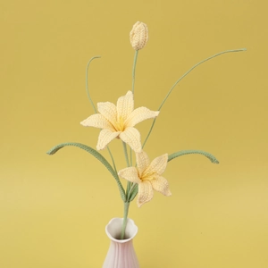 Detailed view of handmade crochet yellow lily flowers with green leaves in a white vase