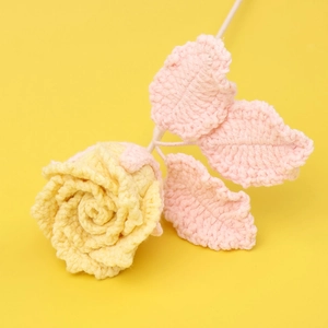 Detail einer handgehäkelten gelben Rose mit zartrosa Blättern auf buntem Hintergrund