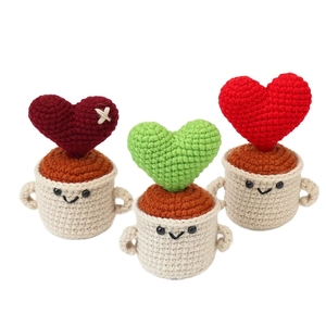 Drei handgestrickte herzförmige Topfpflanzen mit süßen Smileys auf weißen Sockeln
