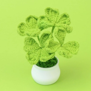 Handmade knitted four-leaf clover plant in a white ceramic pot on a green background