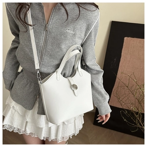 Close-up of white leather tote bag with round metal buckle and adjustable shoulder strap