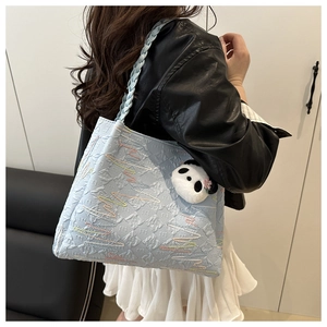 Detail of light blue embossed tote bag with woven shoulder strap and panda pendant
