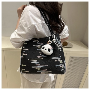 Detail of black canvas tote bag with colorful embroidery and a cute panda plush charm