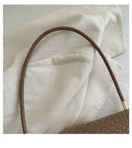 Detail of coffee brown leather bag showing woven handle and embossed texture on fabric