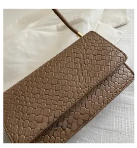 Macro view of woven leather texture on khaki square bag with gold hardware details