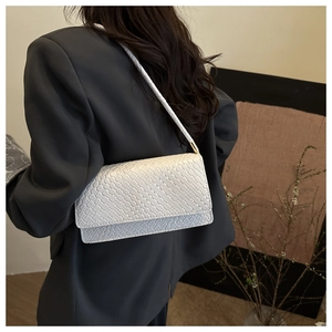 Detail shot of a white woven shoulder bag with golden metal accents on grey blazer