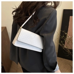 Detail of white faux crocodile texture and metal strap hardware on a chic baguette bag