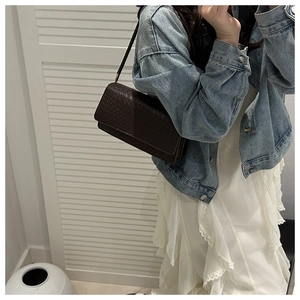 Detail of dark brown woven underarm bag styled with a denim jacket and white skirt