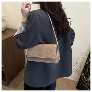 Close-up of beige woven texture and leather details on a shoulder baguette bag