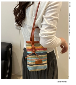 Detail of a colorful striped straw woven crossbody bag with brown leather handles and strap