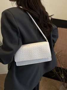 Schicke weiße geflochtene Achseltasche mit goldenen Metallteilen auf grauem Blazer