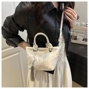 Détail de la broderie florale élégante et du pompon gris sur le sac seau beige chic