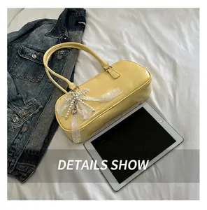 Detalle de bolso de cuero amarillo claro con lazo de encaje blanco y dije de corazón