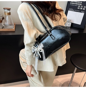 Detalle de bolso de hombro negro brillante con elegante colgante de lazo de encaje y perlas