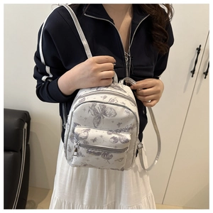 Detail of a mini white backpack with grey butterfly patterns worn over a navy jacket