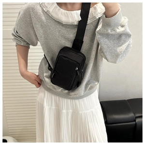 Model wearing a compact black nylon crossbody bag with adjustable wide strap for daily use