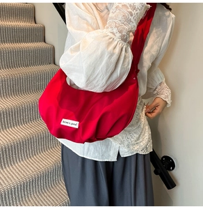 Detail of red crescent dumpling bag featuring Believe in yourself label and wide strap
