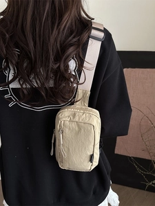 Beige pleated nylon crossbody chest bag with adjustable strap worn by model