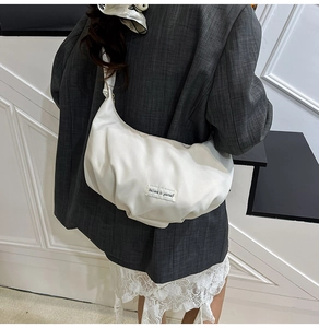 Detail of white pleated crescent bag with Believe in yourself woven label on front