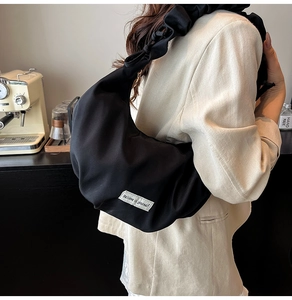 Detail of black crescent shoulder bag with pleated strap and white slogan label