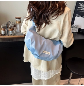 Close-up of light blue crescent dumpling bag with pleated texture and woven label