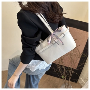 Side view of cream leather tote bag with a checkered bow charm worn by a model