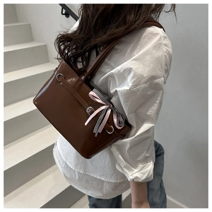 Brown gloss tote bag with pink bow ribbon detail shown from side view on stairs