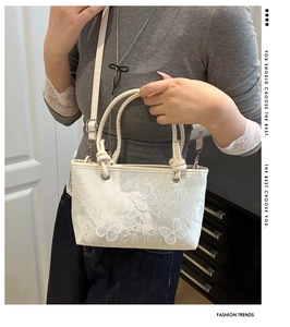 Detail of white lace handbag featuring elegant butterfly embroidery and metal strap hooks