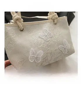 Détail macro de la broderie papillon et texture dentelle sur sac blanc à main
