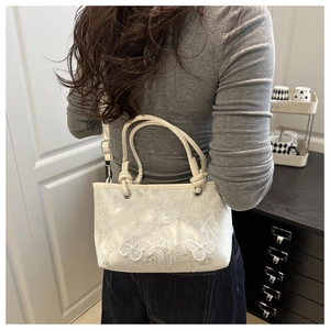 Detail of white bow tote bag with lace butterfly patterns and round handle worn by a model