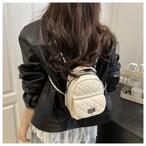 Rear view of model wearing a white quilted mini backpack with woven metal chain straps