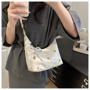 Detail of white glossy shoulder bag with pearl charms, lace bow and gold bone studs