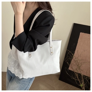 Detail of white crocodile texture tote bag with gold rivets on a model's shoulder