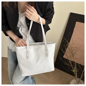 Detail of white crocodile texture tote bag with slim straps and golden rivets