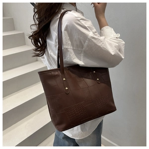 Detailed close-up of dark brown patchwork leather tote bag with elegant gold rivet accents