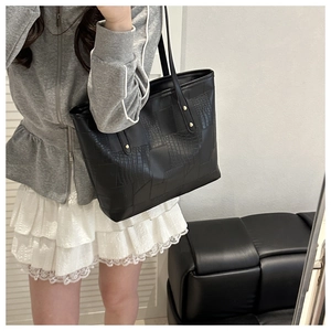 Detail of black crocodile texture tote bag with leather strap and gold metal hardware