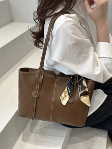 Brown leather tote bag with contrast stitching and decorative scarf on the handle