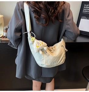 Vue détaillée d'un sac demi-lune en nylon beige avec breloque étoile sur l'épaule du mannequin