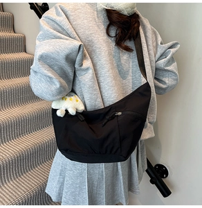Modèle portant un sac bandoulière croissant en nylon noir avec bandoulière et breloque