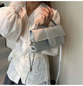 Detail of silver metallic handbag with FASHION lettering and pearl bow charm accessory
