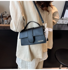 Detail of black leather handbag with pearl charm and lace bow in a city street setting