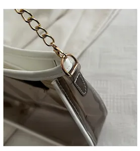 Detail of transparent PVC shoulder bag with white edges and gold metal chain link