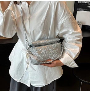 Detail van zilveren crossbodytas van reliëfleer met metalen ketting en parel-kant hanger
