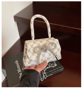 Detailed shot of mini handbag with rhinestone bow, logo pattern, and silver chain strap