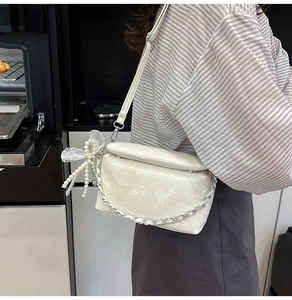 Detail van crème tas met slangenprint, parelhanger en zilverkleurige metalen ketting