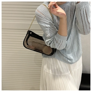 Detail of black transparent jelly shoulder bag with gold chain strap and stylish items inside