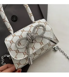 Detail of white mini square bag with brown cat patterns and sparkling crystal bow