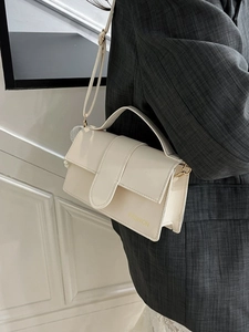 Elegant cream rectangular crossbody bag with top handle and gold letter print on model